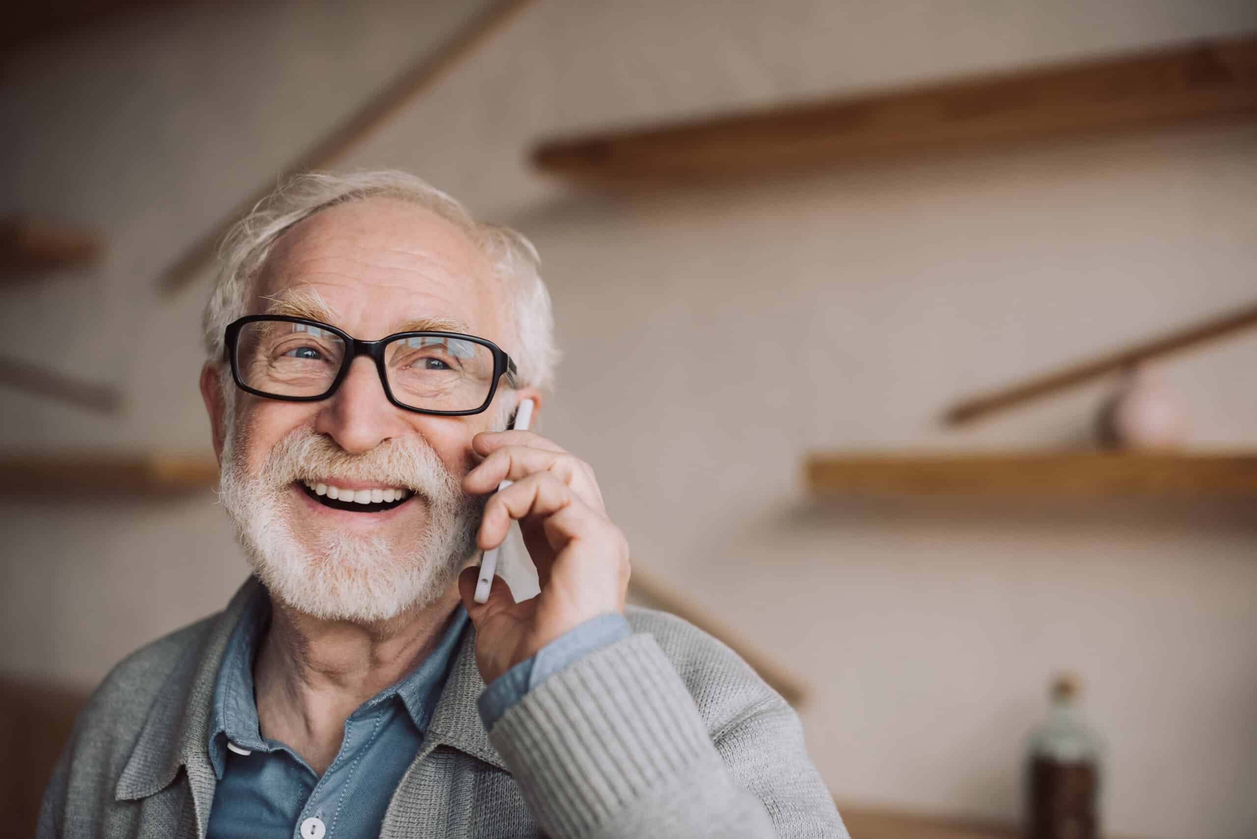 Homme senior souriant parlant au téléphone pour aide pour maison de retraite dans un intérieur chaleureux