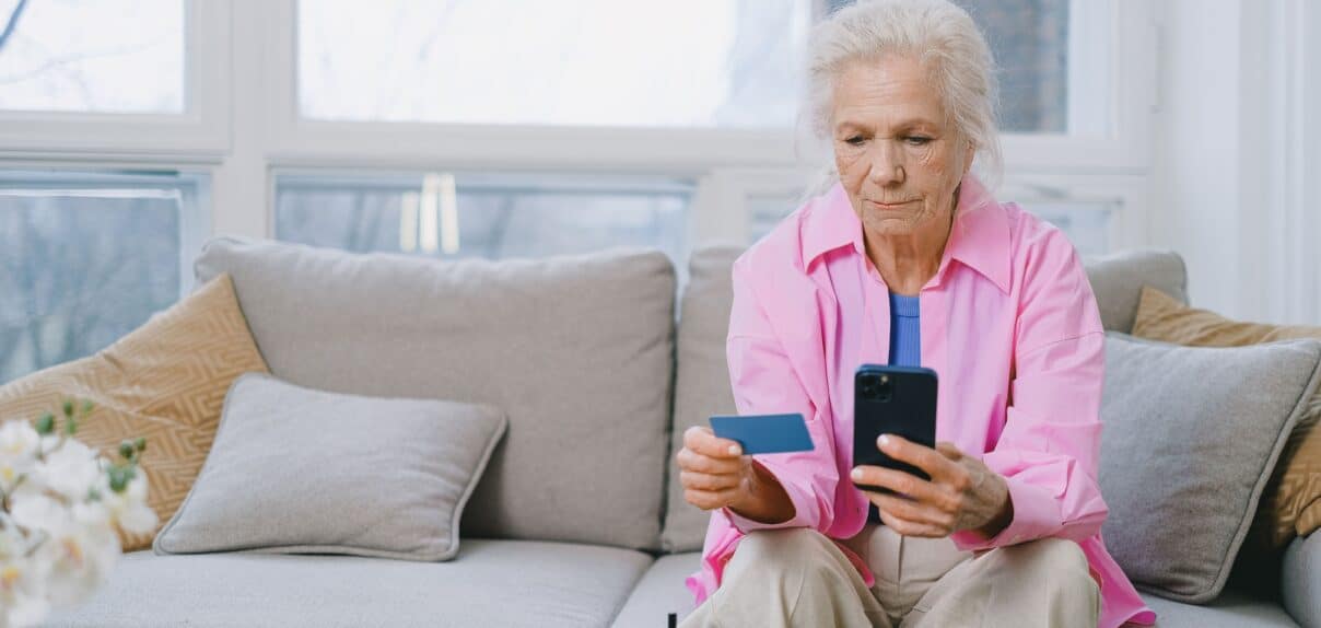 Une senior assise tenant son téléphone et sa carte bancaire en appel avec un hacker