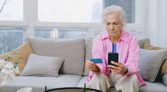 Une senior assise tenant son téléphone et sa carte bancaire en appel avec un hacker