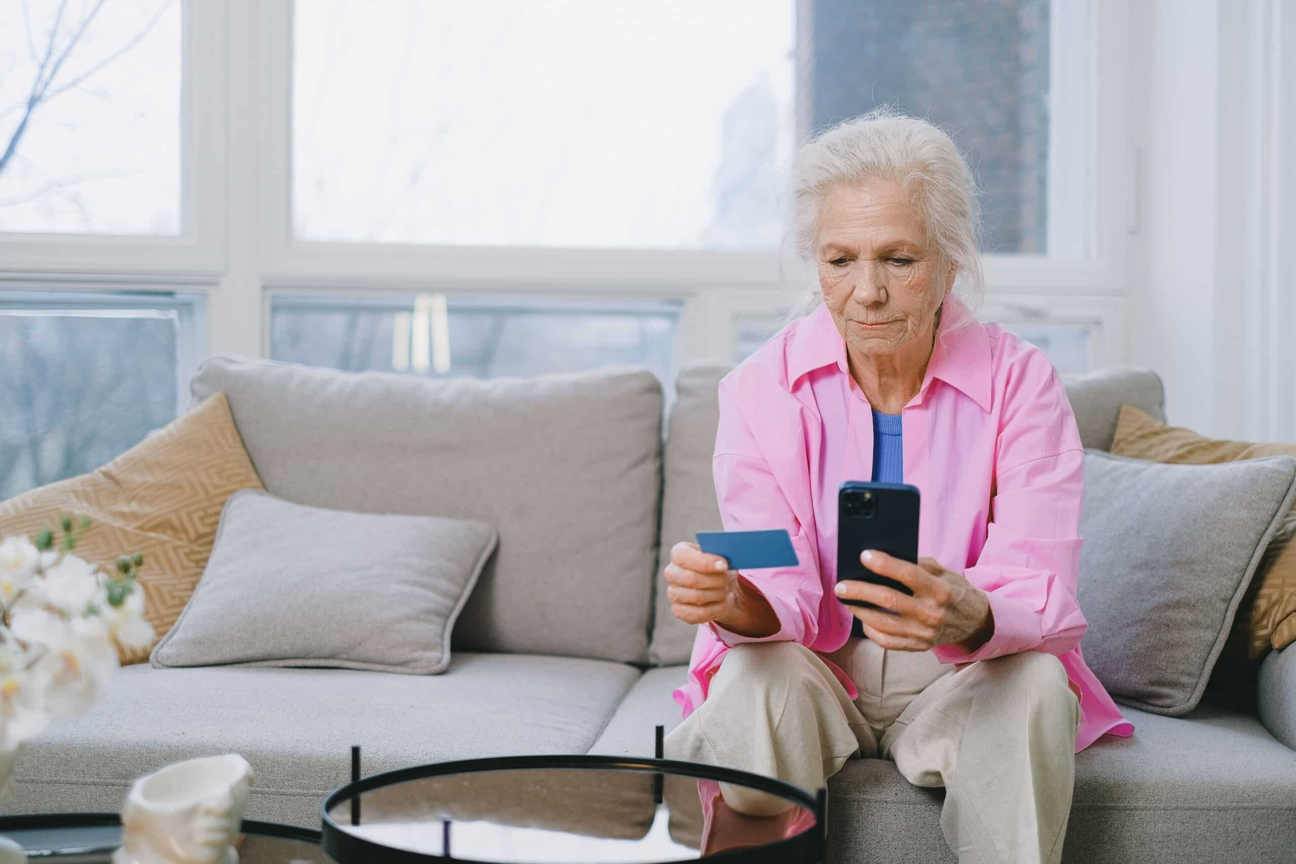 Une senior assise tenant son téléphone et sa carte bancaire en appel avec un hacker